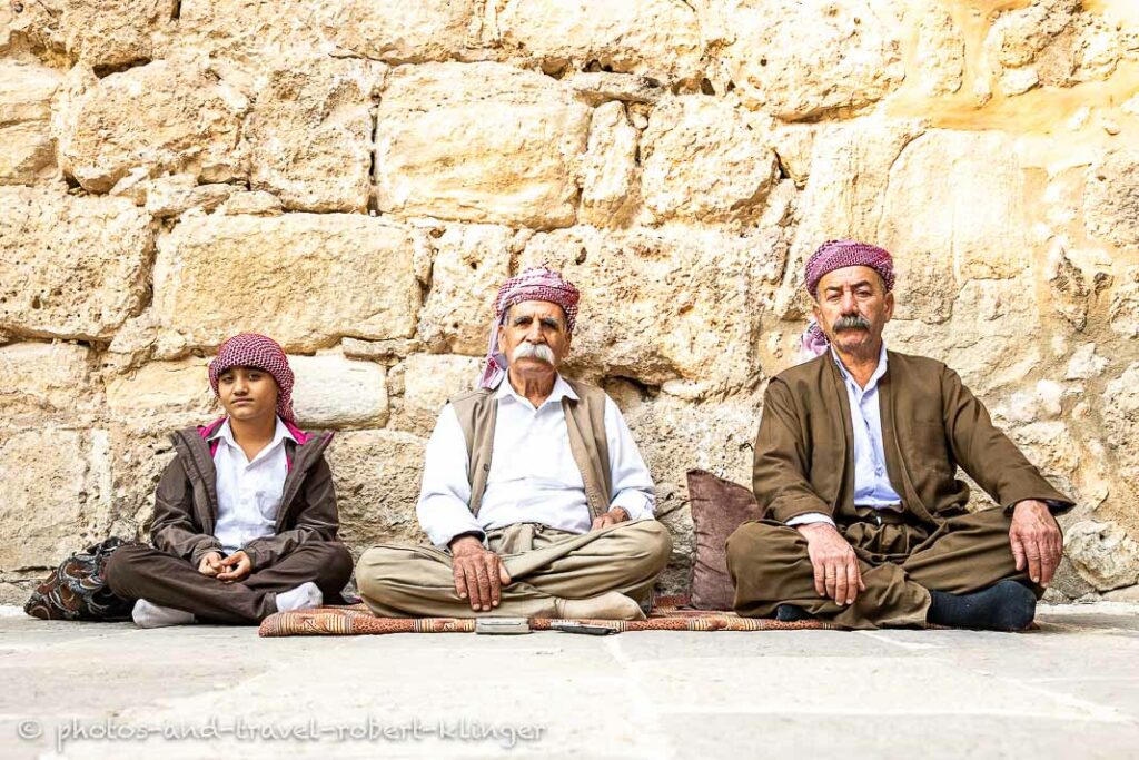 Two men and a boy sitting in front of the Tomb of Sheikh ʿAdī in the Lalish valley