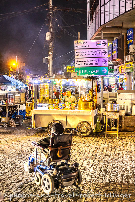 A man in a wheelchair crossing the road in Erbil in front of a street restaurant